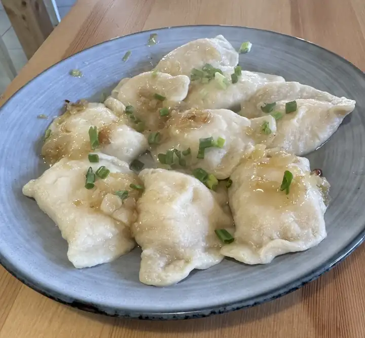 Talerz pierogów polanych masłem, posypanych szczypiorkiem, na drewnianym stole
