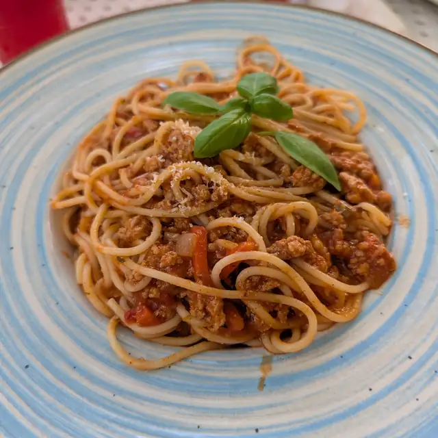 Spaghetti w sosie mięsno-pomidorowym z listkiem bazylii na niebieskim talerzu